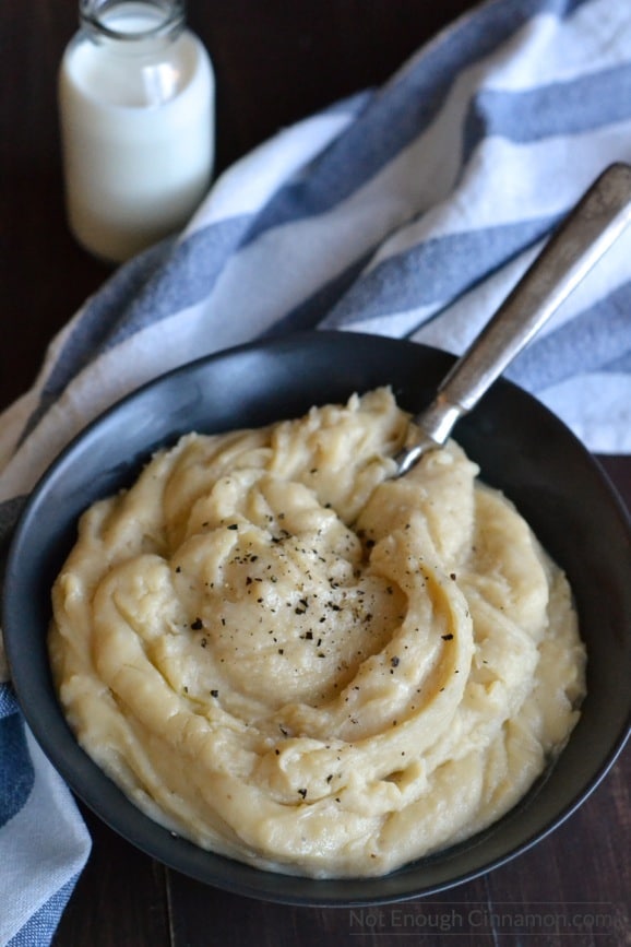 overhead shot of slow cooker mashed potatoes with goat cheese served in a matte black bowl with some cracked pepper on top