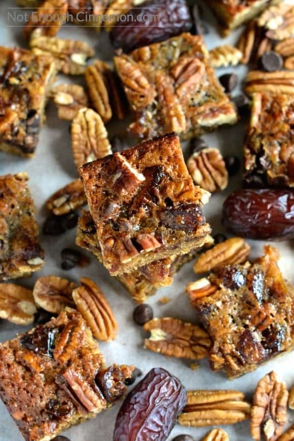 overhead shot of healthy pecan date bars stacked on a baking tray with some dates and whole pecans in between