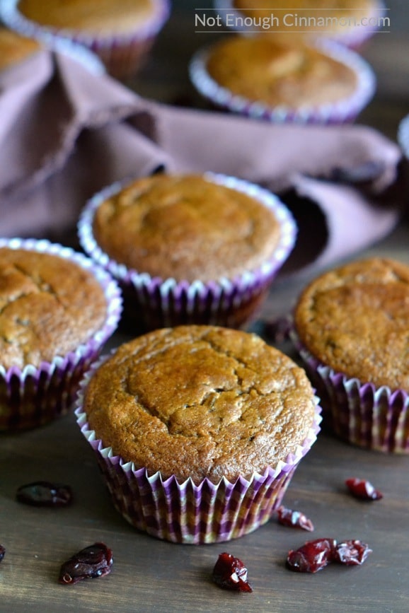 healthy pumpkin muffins studded with dried cranberries on a wooden table with a purple napkin in the background and dried cranberries on the side