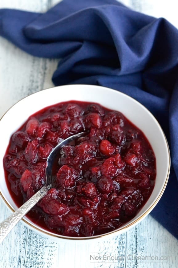 a white bowl of homemade cranberry sauce with orange juice on a rustic white table with a blue napkin in the background
