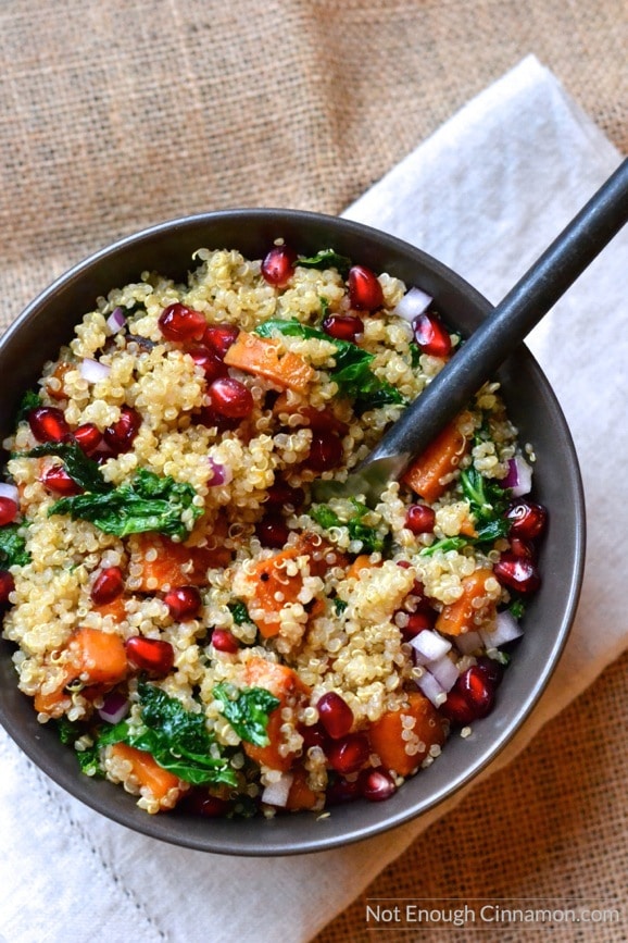 overhead shot of a bowl of warm quinoa & sweet potato kale salad with pomegranate arils sprinkled on top 