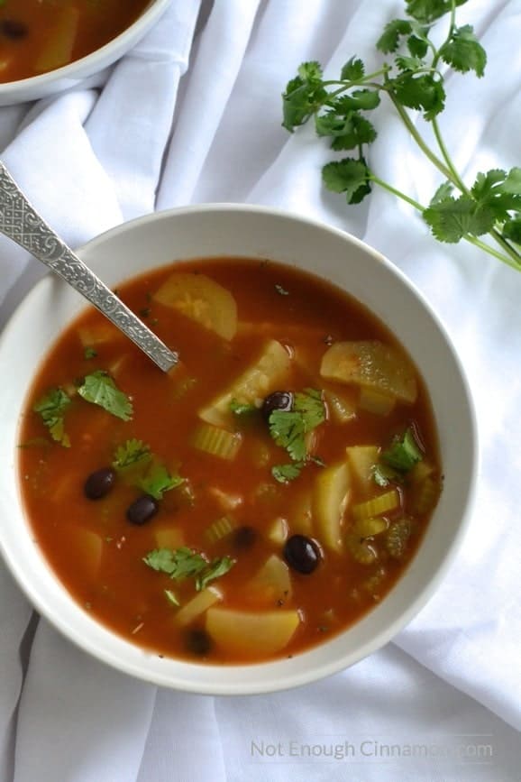 overhead shot of a bowl of veggies soup with sliced zucchinis and black beans in a healthy tomato broth 