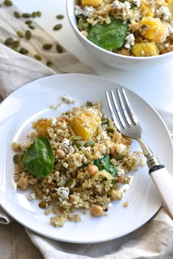 a white plate with easy Quinoa Salad with chickpeas, roasted squash, spinach and pepitas with a fork on the side