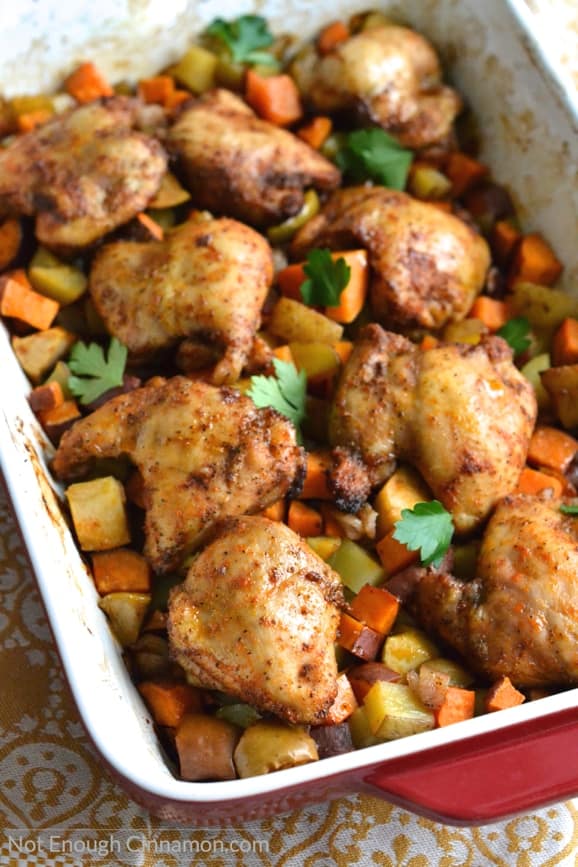 a One Pan Chicken Dinner of BBQ spiced chicken thighs on chunks of roasted root vegetables and apples in a red casserole dish 
