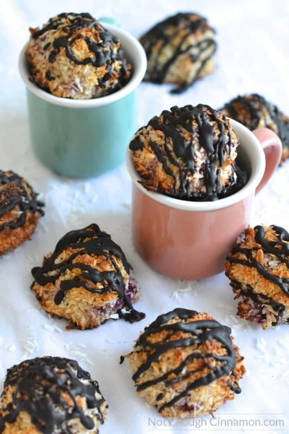 Refined sugar free chocolate coconut macaroons with raspberries arranged in and around two pasted coloured espresso cups