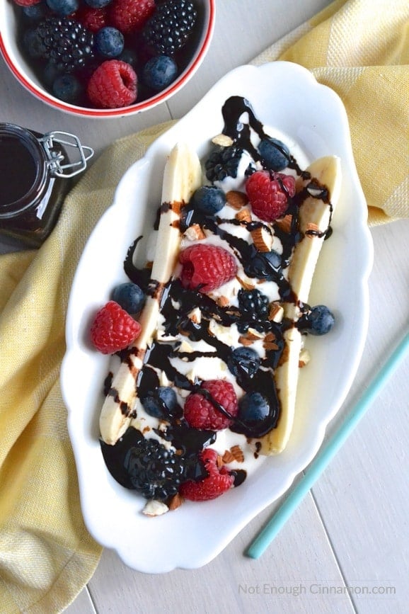 healthy banana split filled with frozen yogurt, berries and drizzled with sugar-free homemade chocolate sauce on a white oval bowl 