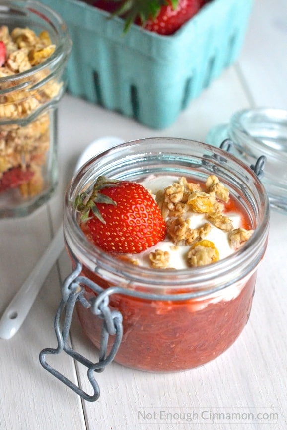 a mason jar with Rhubarb and strawberry chia pudding breakfast topped with granola, greek yogurt and a strawberry