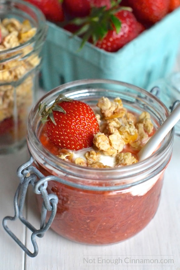 close-up of rhubarb and strawberry chia pudding breakfast cup topped with granola, yogurt and a fresh strawberry