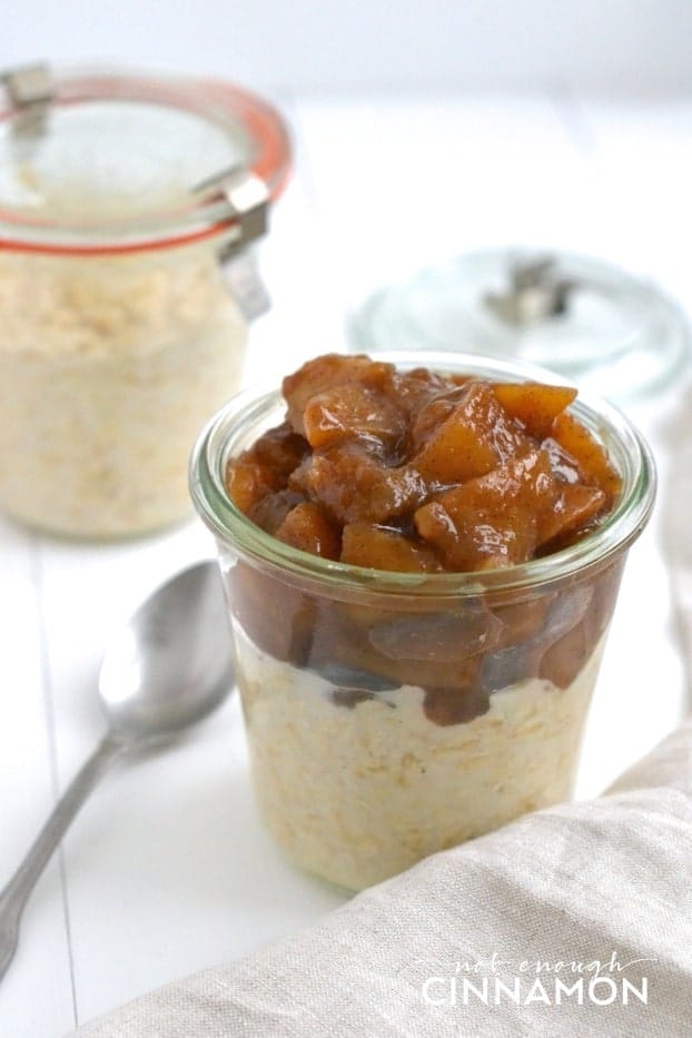 Clean Eating Apple Pie Overnight Oats with caramelized apple cinnamon topping served in two small mason jars with a spoon on the side