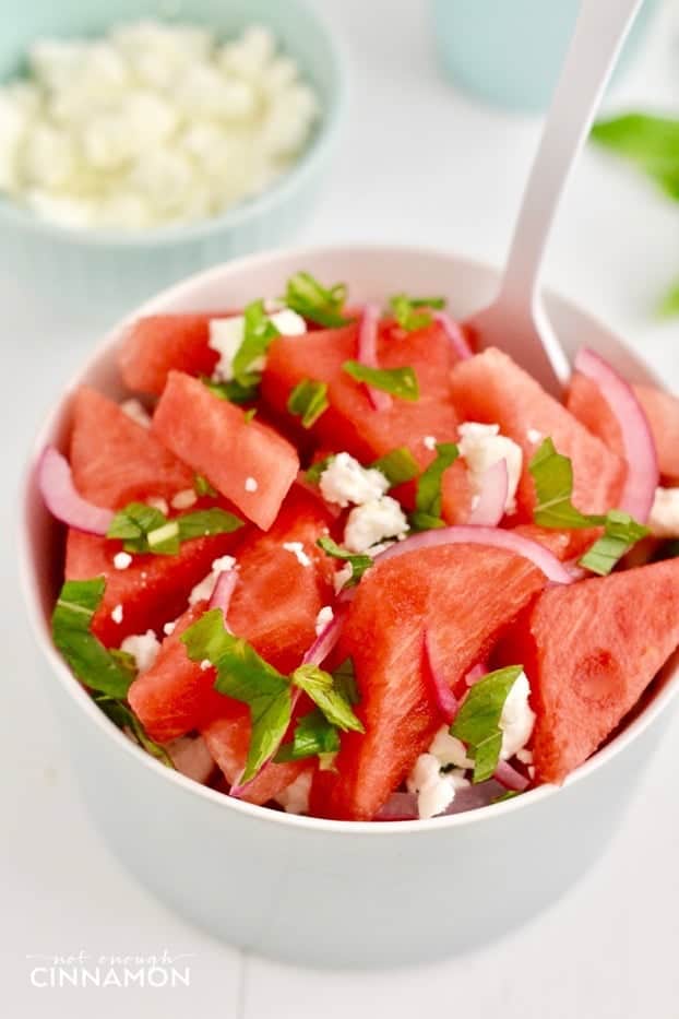 close-up of watermelon salad with feta and mint in a white bowl with a spoon 