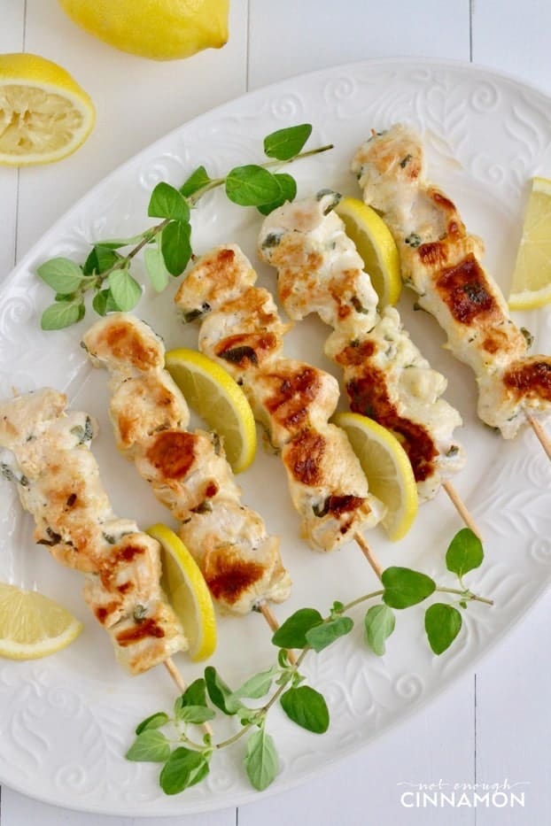 overhead shot of Greek Lemon Chicken Skewers on a white serving plate with lemons in the background