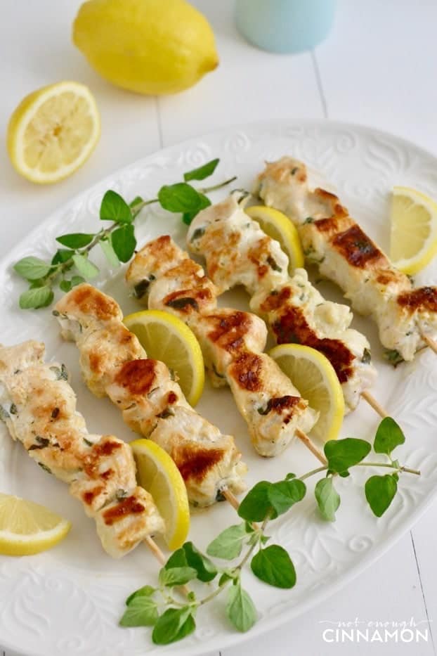 Greek Lemon Chicken Skewers on a white plate with fresh oregano and lemon slices