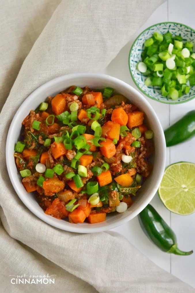 overhead shot of paleo no bean beef and sweet potato chili in a white bowl with sliced scallions and green chilies on the side