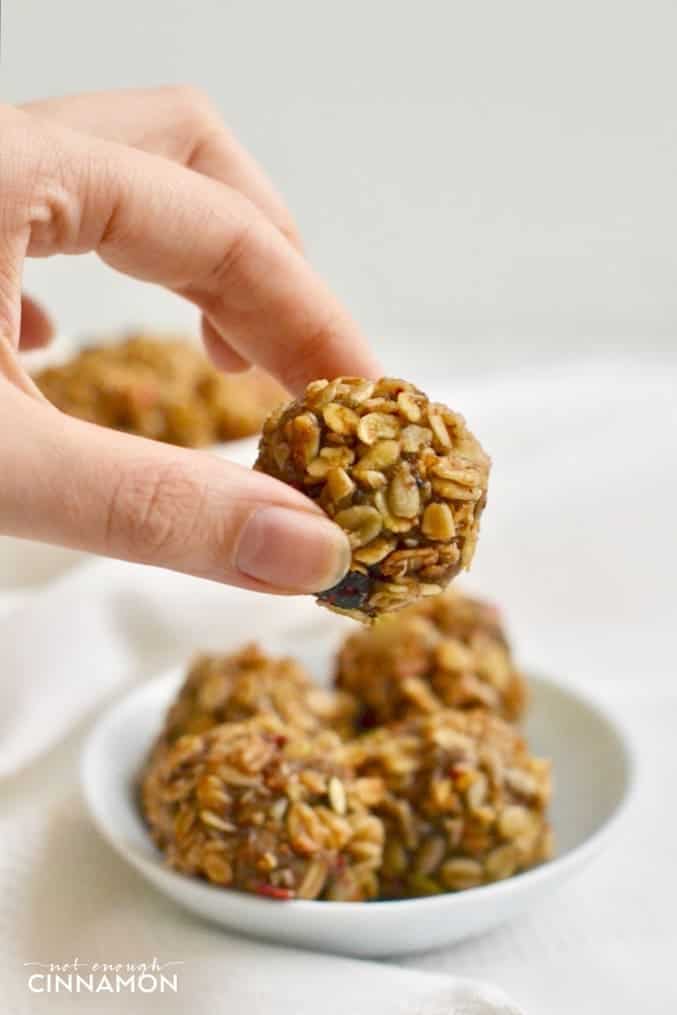 a hand holding a Healthy No Bake Granola Bite with a small plate of granola bites in the background