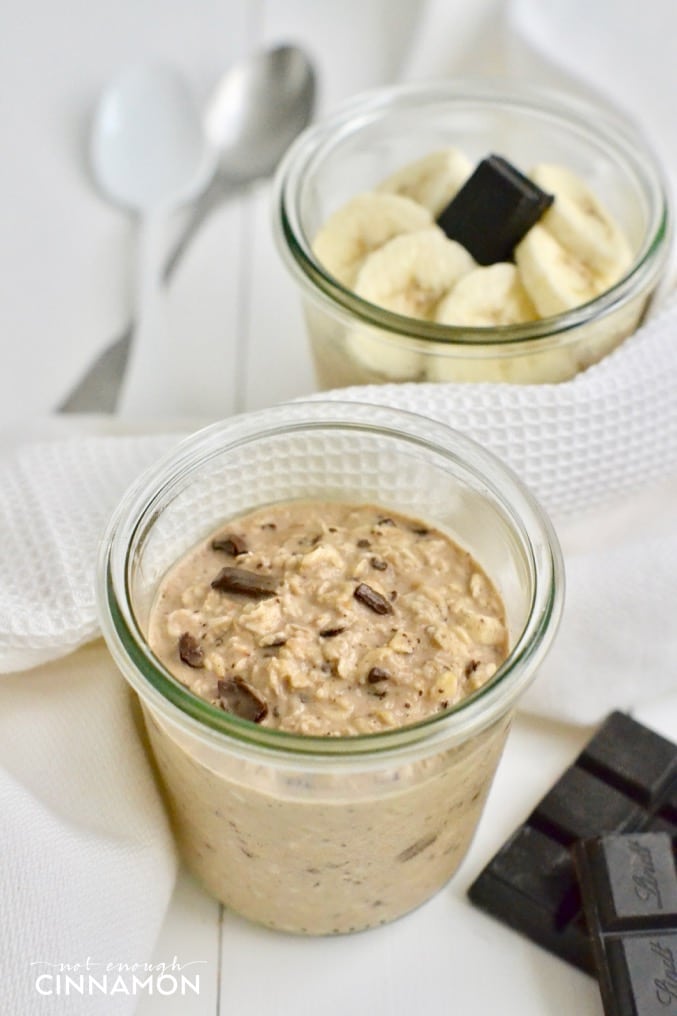 Healthy Peanut butter and chocolate overnight oats served in a mason jar with chocolate shavings on top and sliced bananas in the background
