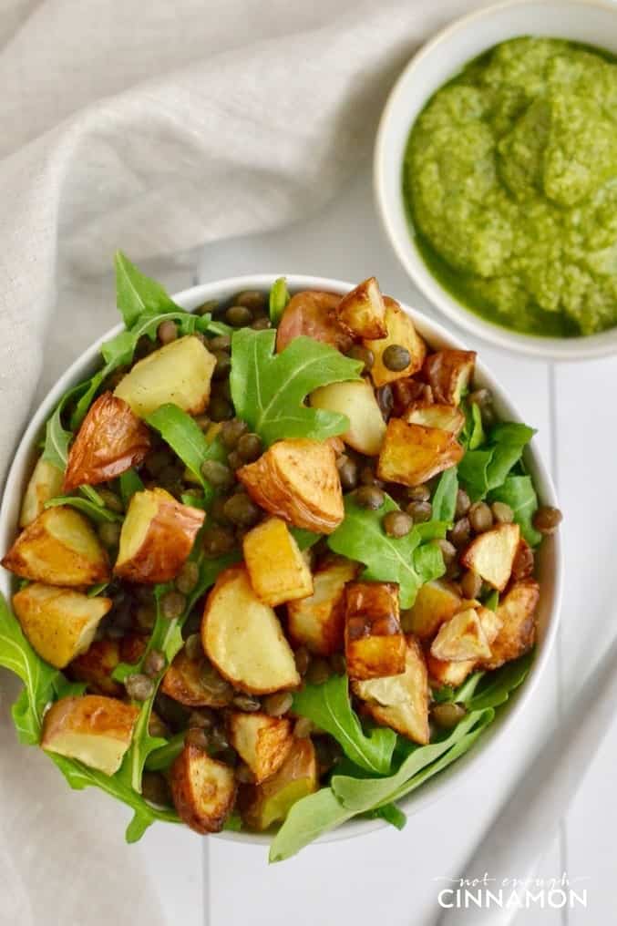 overhead shot of arugula, roasted potato and lentil salad with a side dish of homemade lemon walnut pesto on the side 