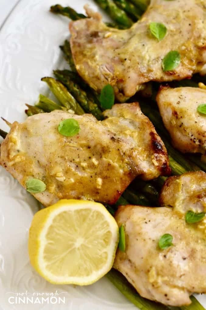 close-up of clean eating baked maple mustard chicken thighs served on green asparagus on a white platter 