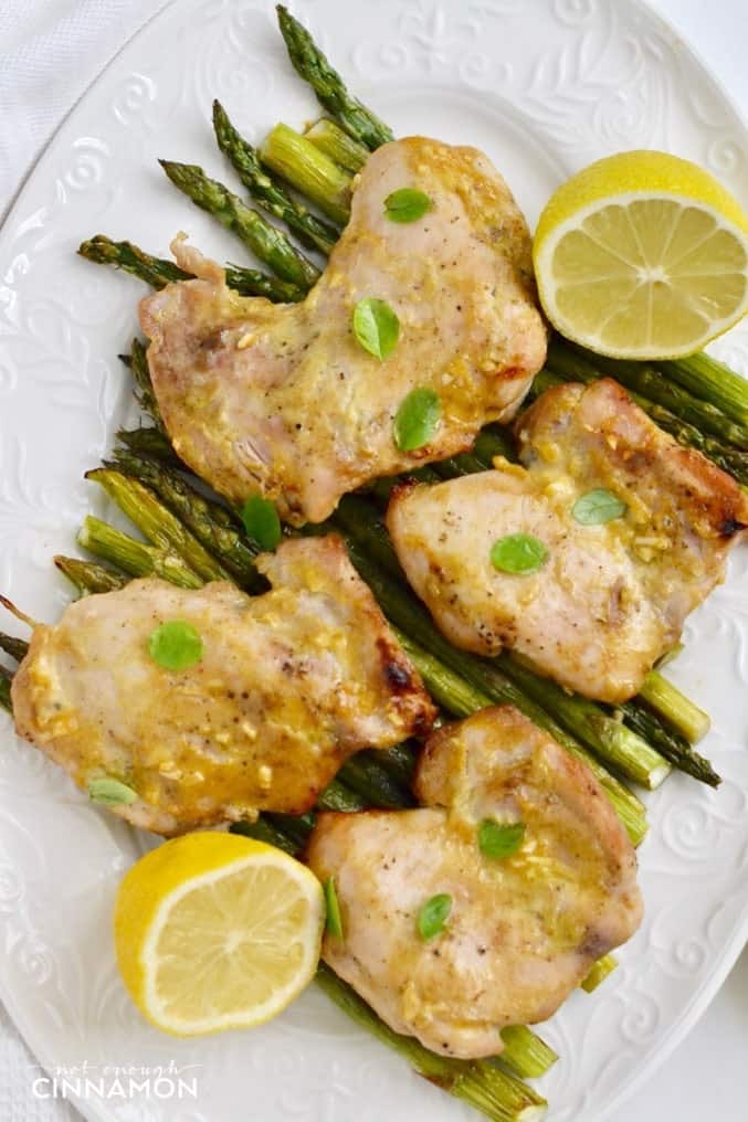 overhead shot of a white platter of baked maple mustard chicken thighs on green asparagus 