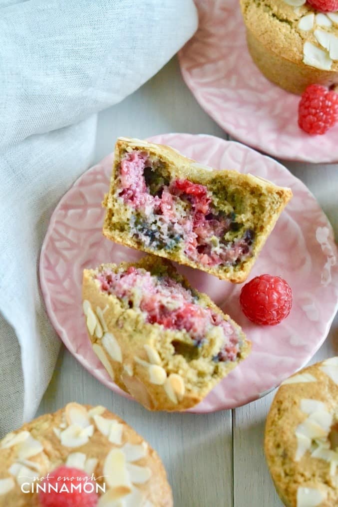 a healthy raspberry almond muffin broken in two halved on a pink plate