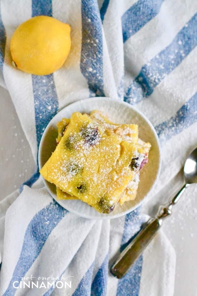 overhead shot of a plate of healthy blueberry lemon bars dusted with icing sugar on a striped dishtowel 