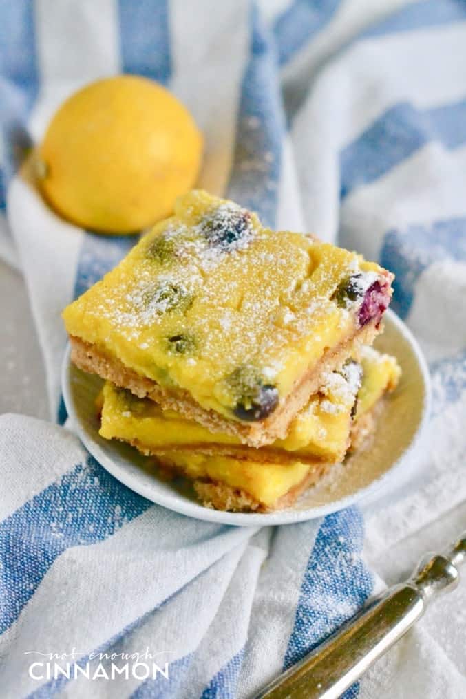 side view of a stack of healthy blueberry lemon bars on a small white plate with a lemon in the background