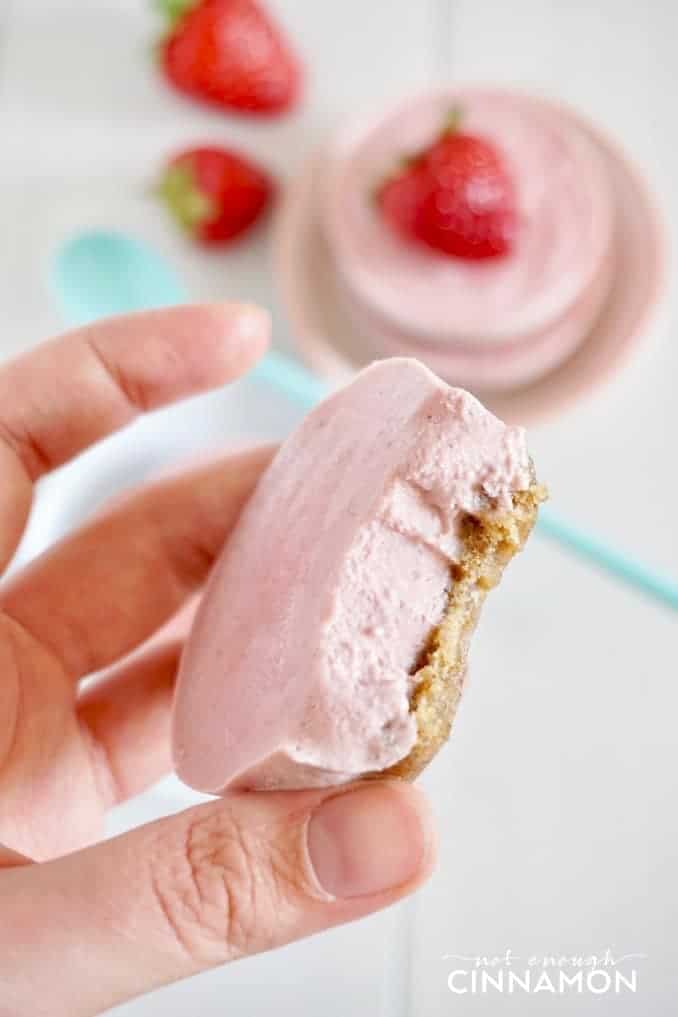 a hand holding a bite-sized Vegan Strawberry Cheesecake with one bite missing