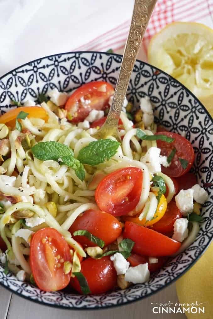 close-up of a bowl of zucchini noodle salad with tomatoes, feta, mint and pistachios