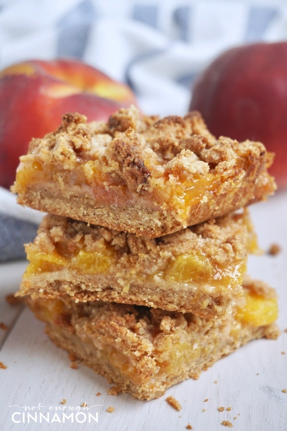 side view of three stacked healthy peach crisp bars with peaches in the background
