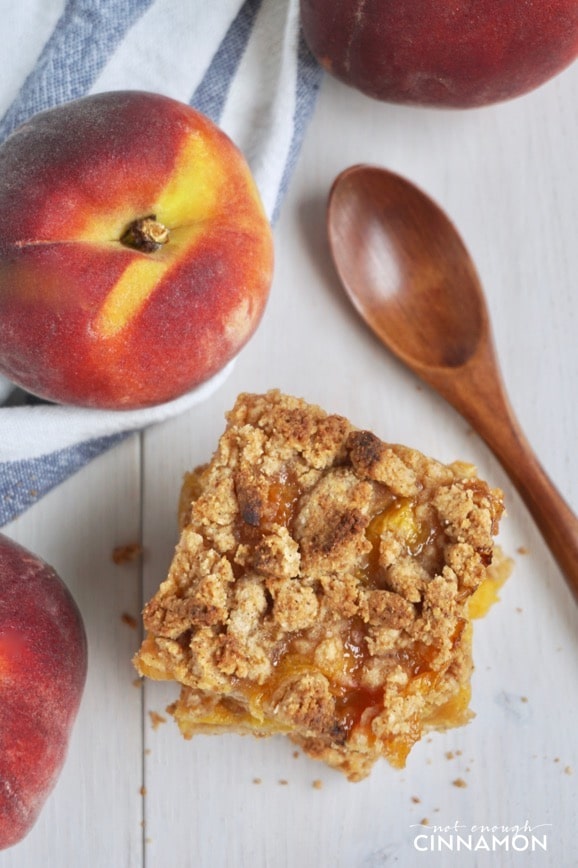 overhead shot of stacked healthy peach crisp bars next two fresh peaches 
