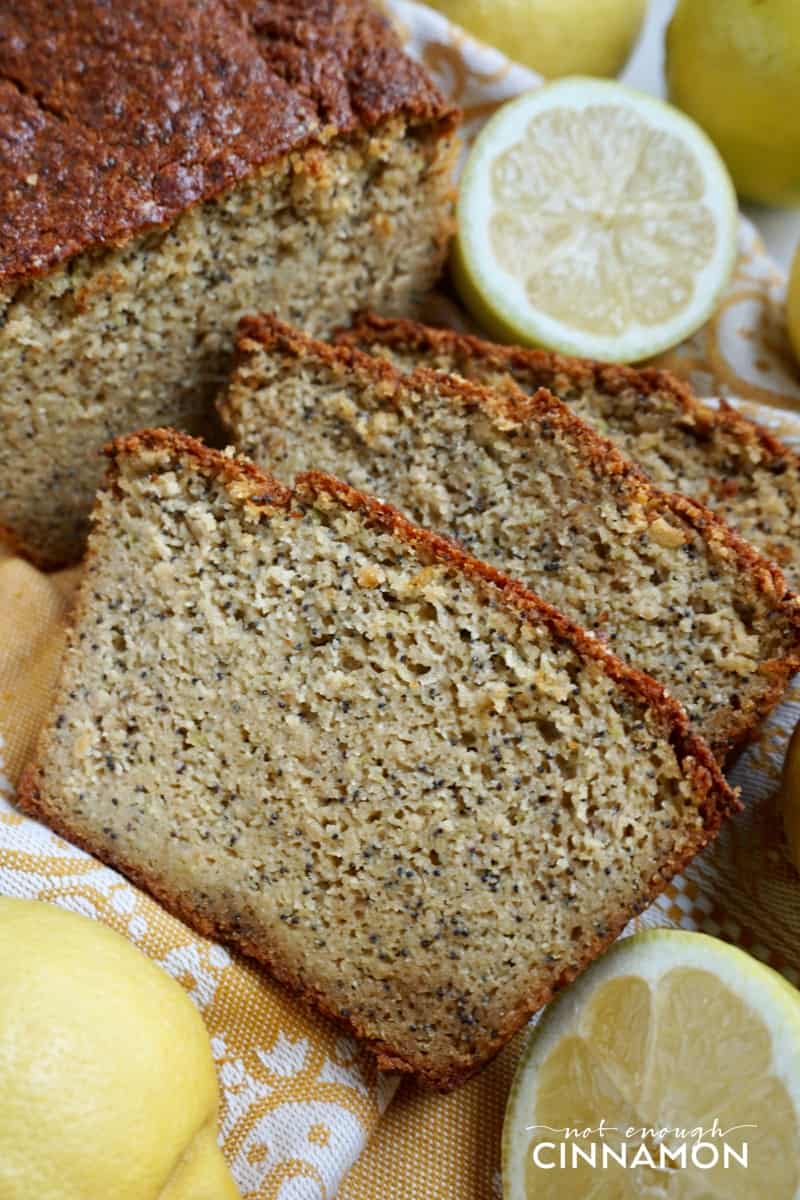 three slices of moist paleo zucchini bread with lemon and poppy seeds with halved lemons on the side