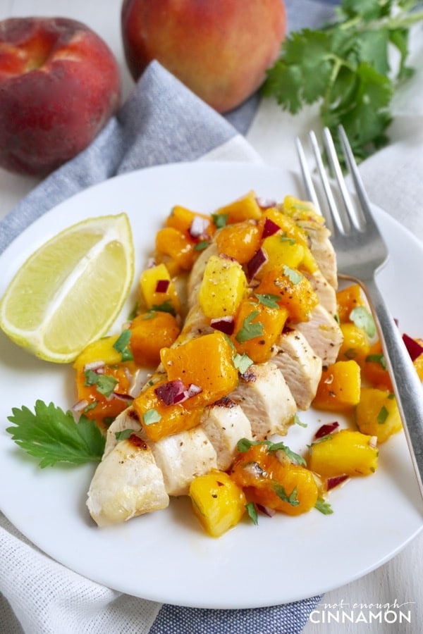 grilled chicken breast topped with peach mango salsa on a white plate