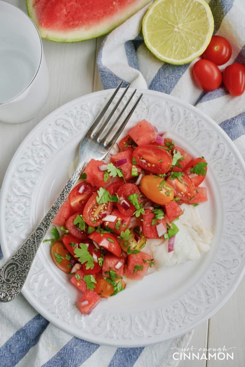 white fish fillet topped with tomato watermelon salsa on a white plate