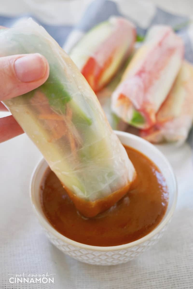 a vegan summer roll being dipped into a small dish with Thai peanut sauce