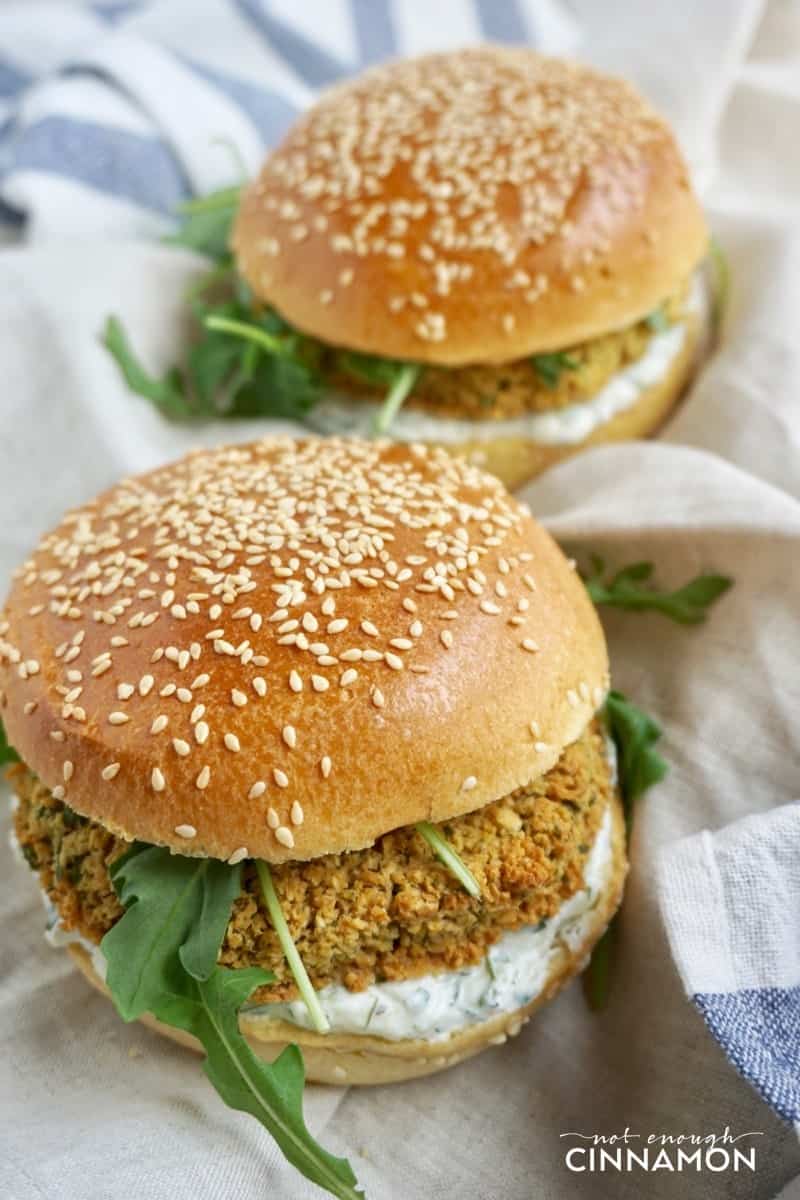 two vegetarian falafel burgers with falafel patties, tzatziki, and fresh arugula on a striped kitchen towel