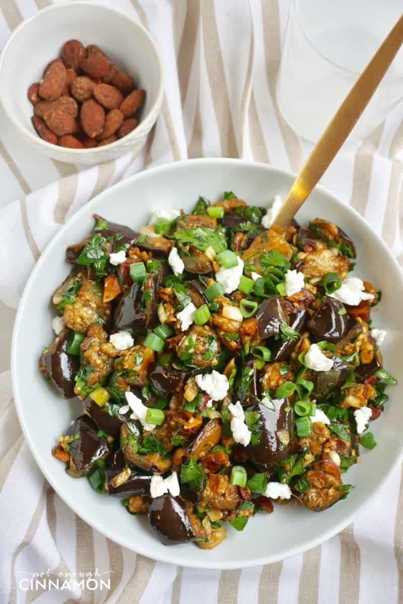 overhead shot of roasted eggplant salad sprinkled with crumbled feta and smoked almonds