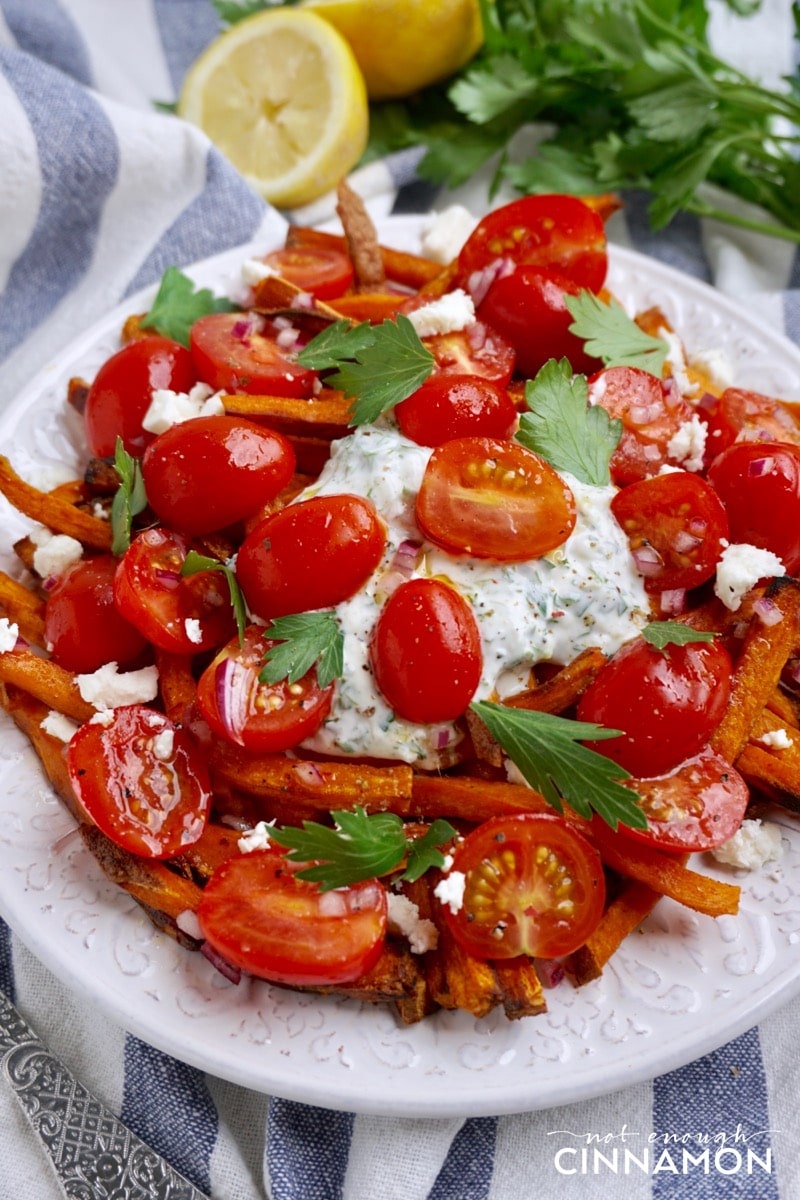 side view of a plate of Loaded Sweet Potato Fries topped with tzatziki, feta and tomato salad. 