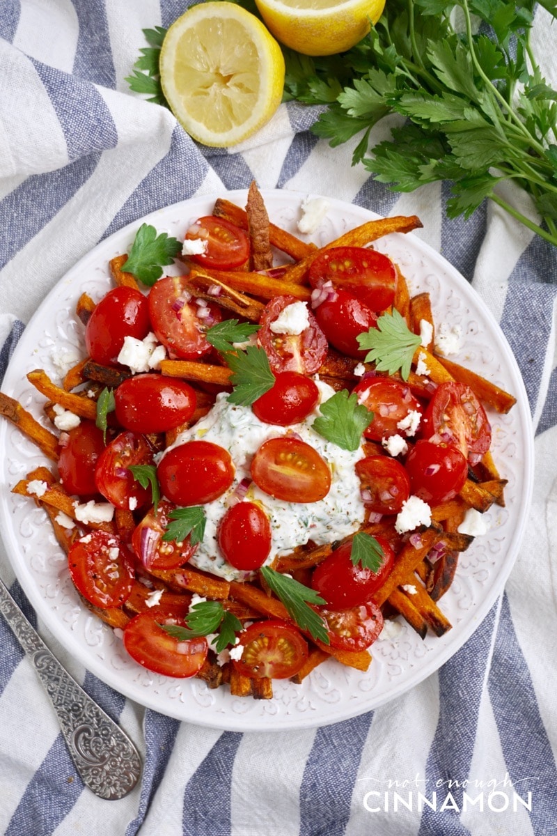 a plate of Loaded Sweet Potato Fries topped with Greek tzatziki, feta and tomato salad