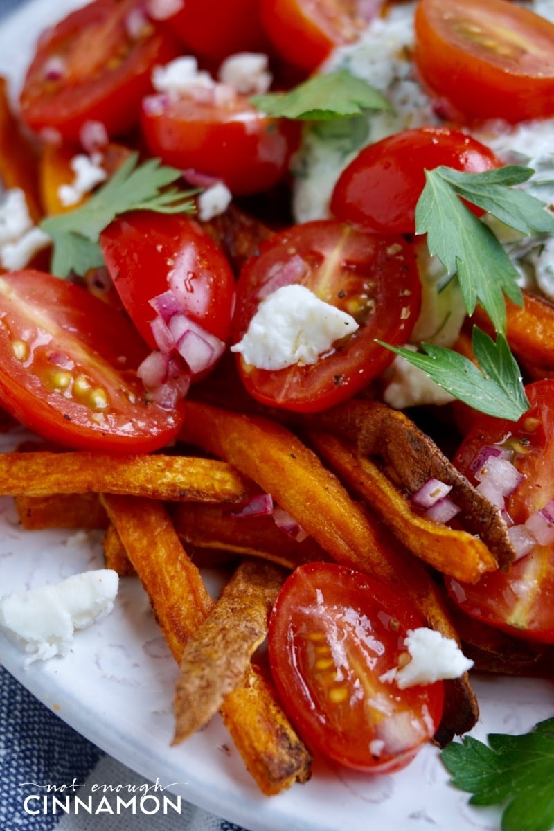 close-up of vegetarian Loaded Sweet Potato Fries with tzatziki, feta and tomato salad. 