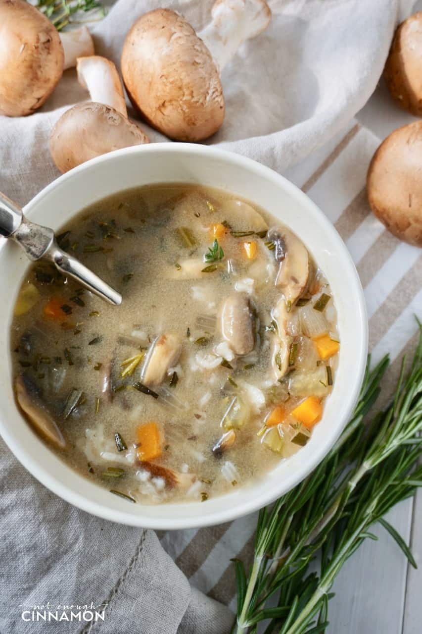 overhead shot of a bowl of mushroom and rice soup with cremini mushrooms in the background