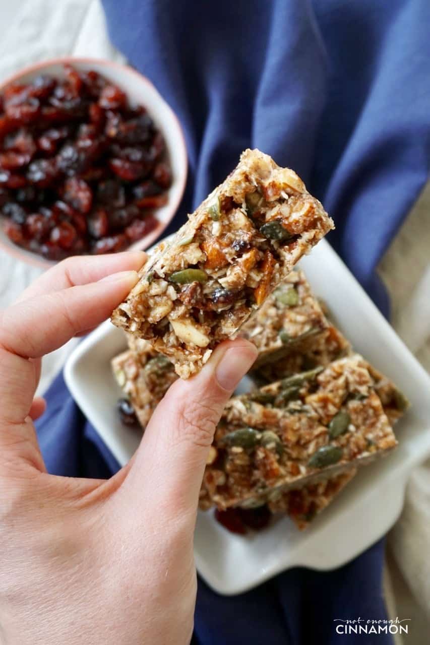 a hand holding a No Bake Cranberry Pumpkin Spice Snack Bar over a plate of bars