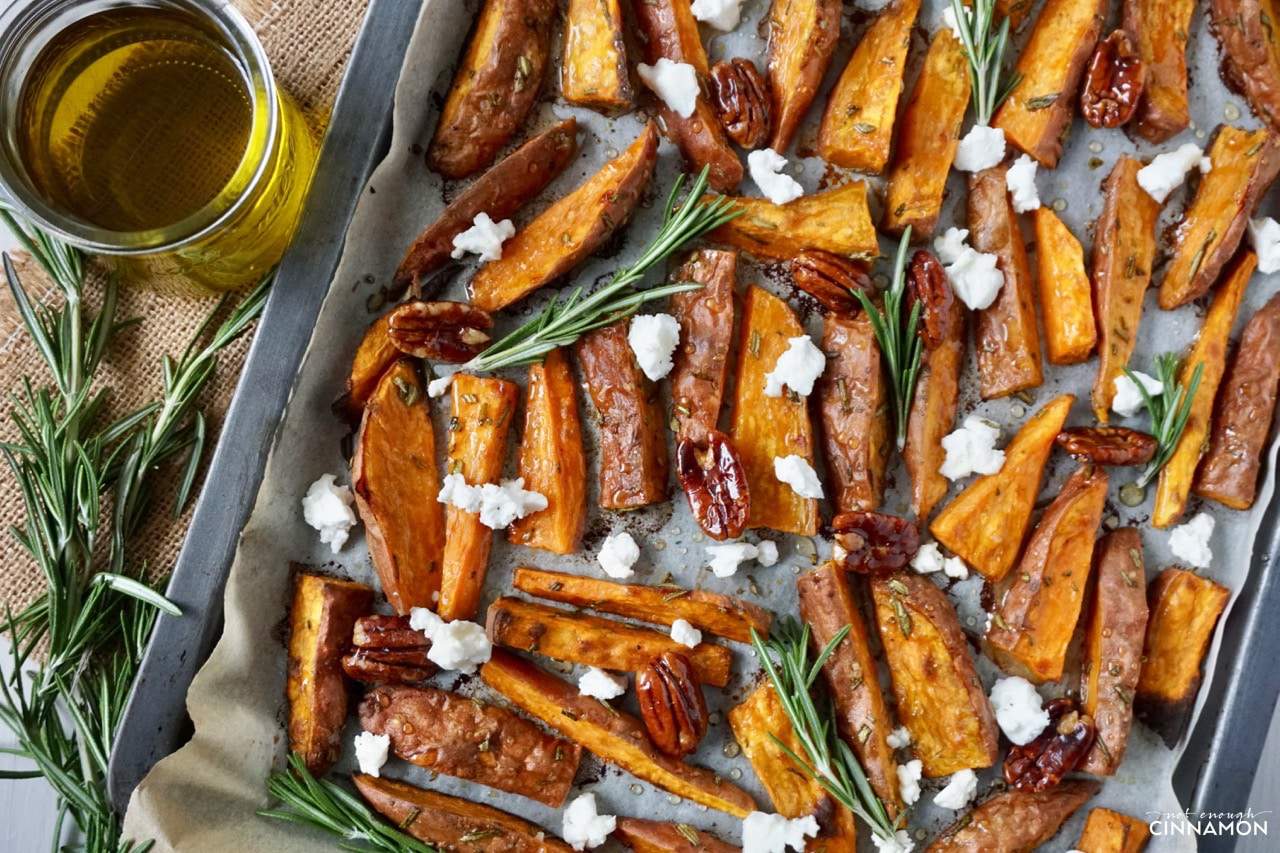 overhead shot of Sweet potato wedges on a baking sheet drizzled with olive oil, goat cheese and candied pecans 