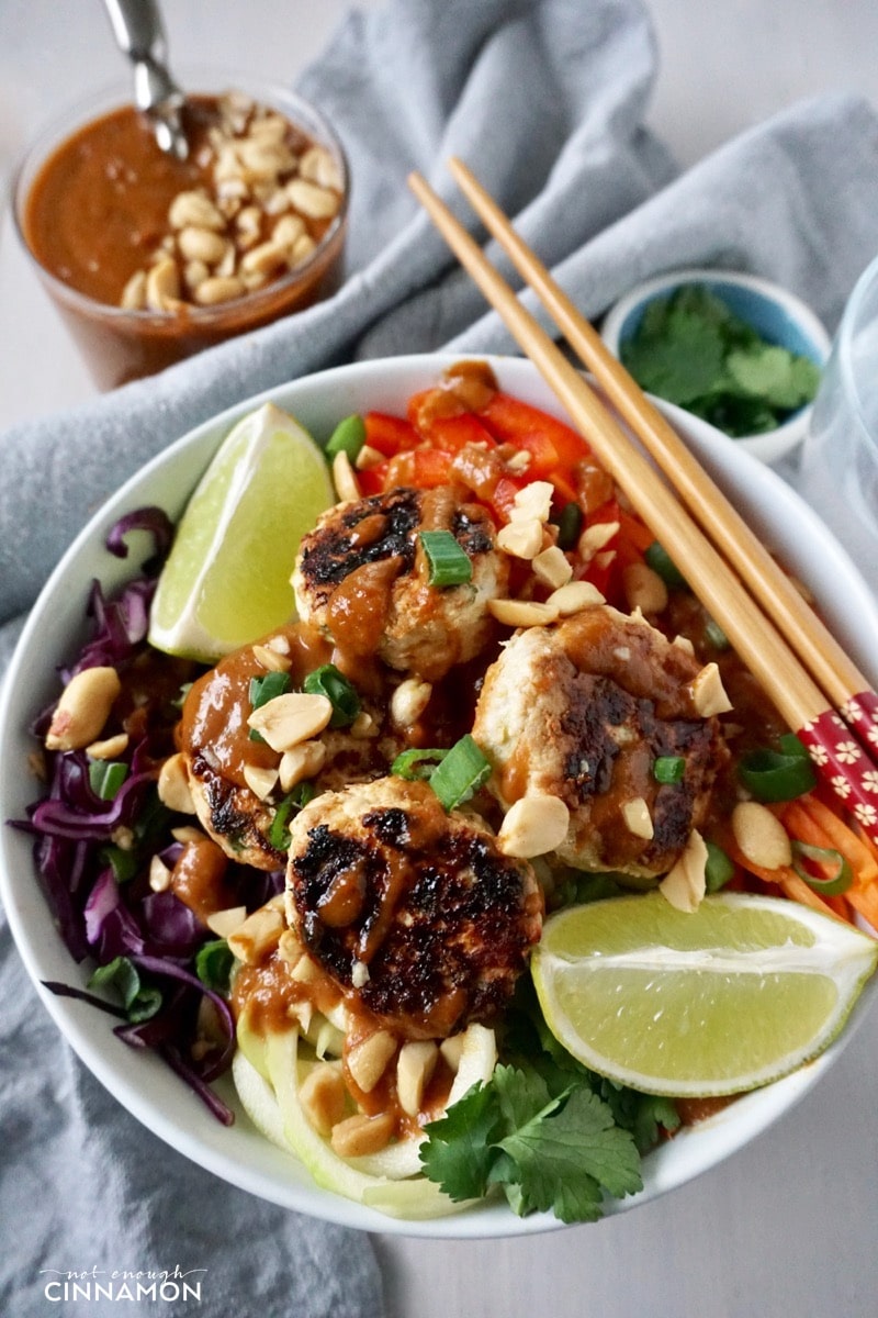 close-up of a Thai veggie bowl with veggie noodles and mini Thai chicken patties drizzled with peanut sauce