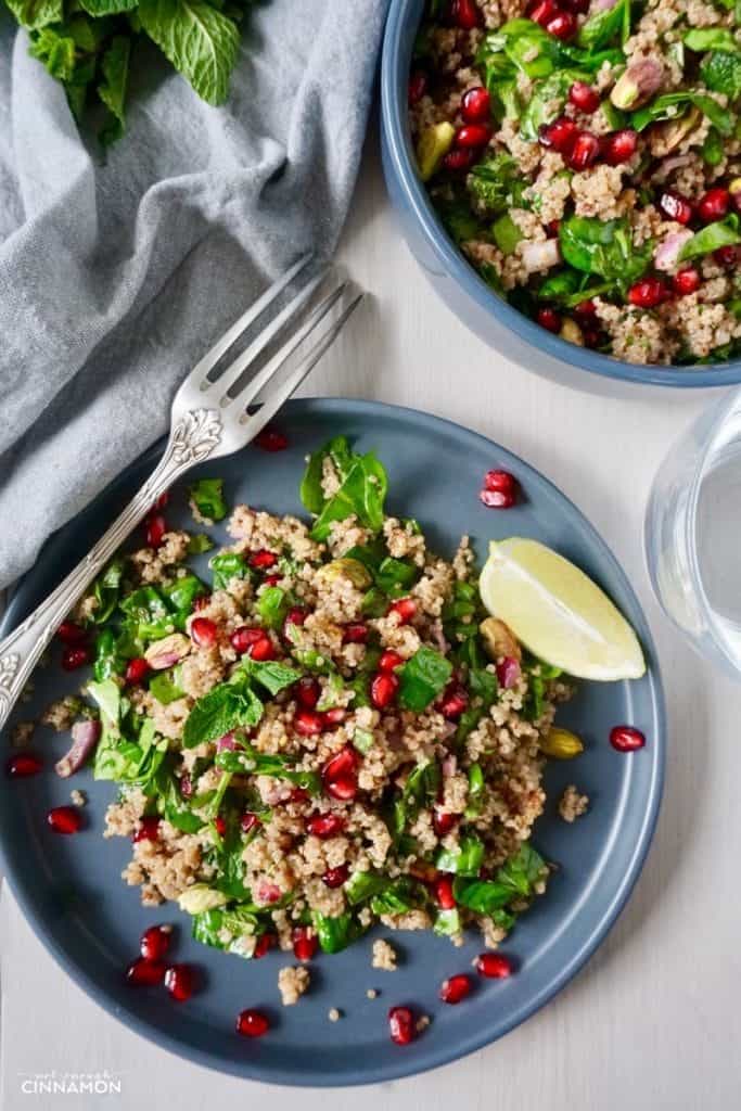 vegan quinoa salad with spinach, mint, pistachios and pomegranate arils on a blue plate