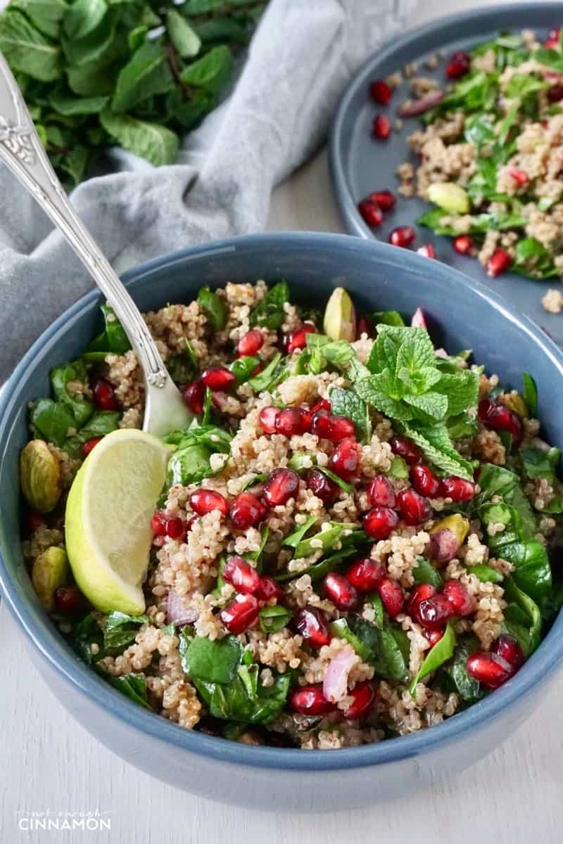 A beautiful Persian vegan quinoa salad with spinach, mint and pomegranate arils in a blue bowl