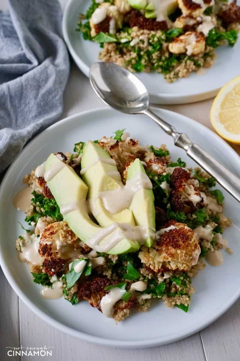 a plate full of oven-roasted cauliflower, quinoa, kale and avocado slices, topped with tahini sauce