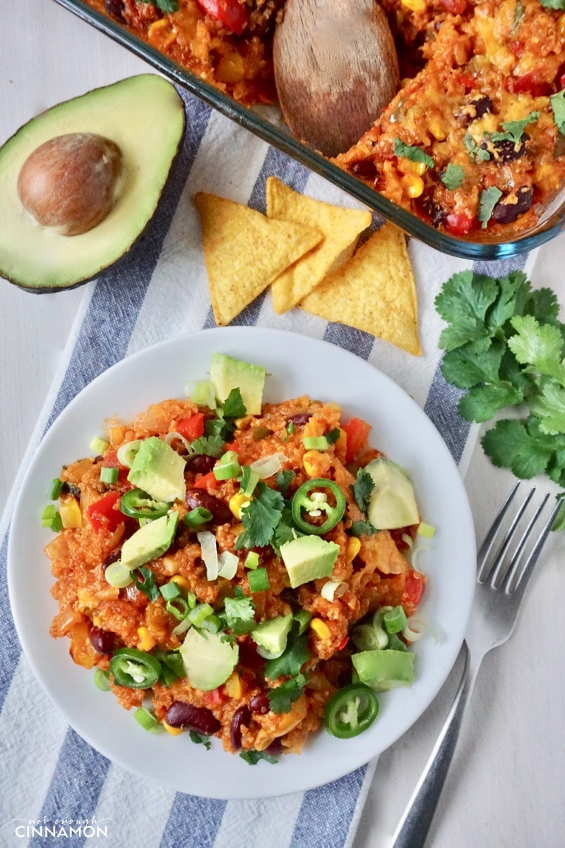 overhead shot of a plate with Mexican quinoa casserole with a casserole dish, nacho chips and an avocado in the background