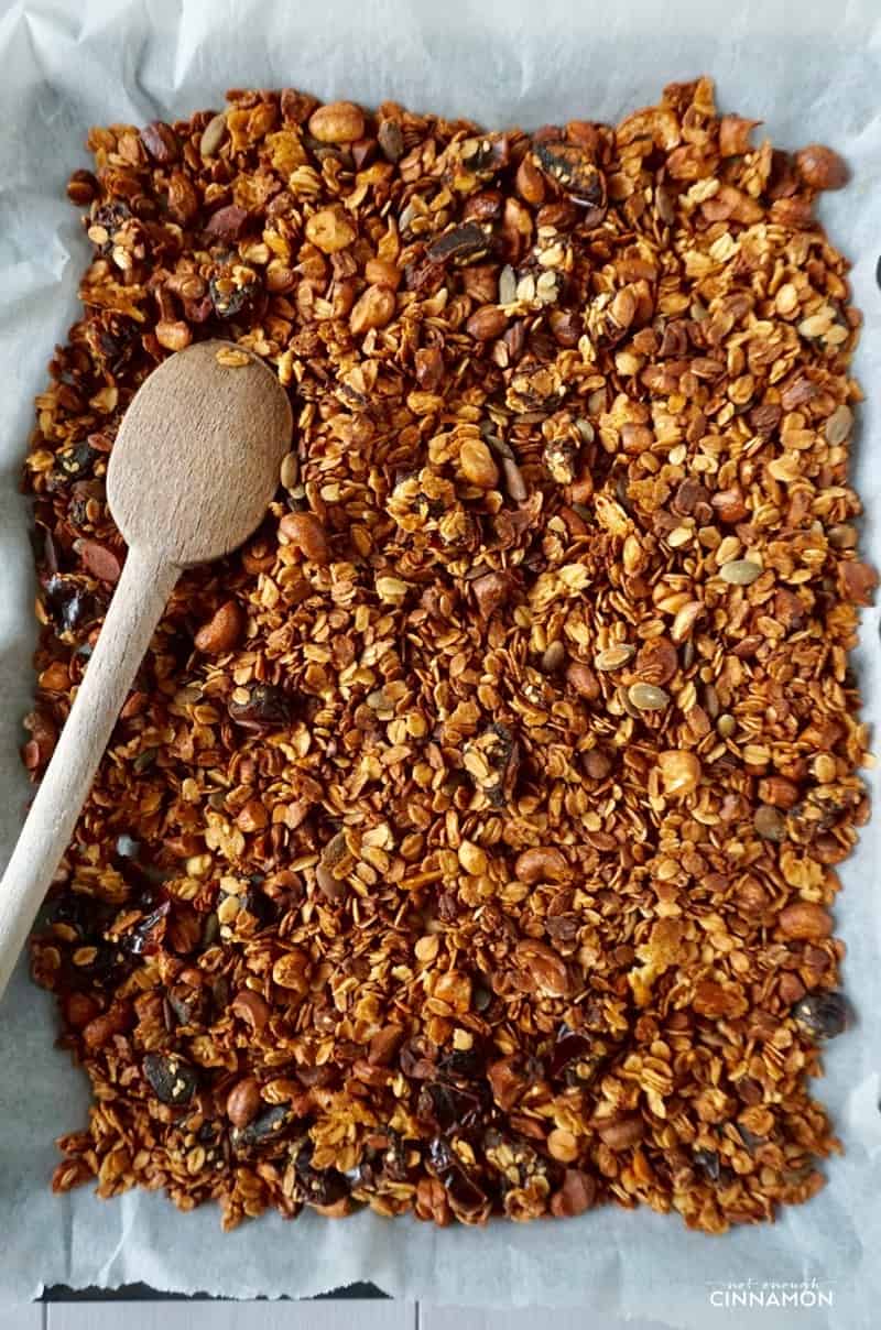 baked honey granola with dates and cashews being stirred with a wooden spoon on a baking sheet 