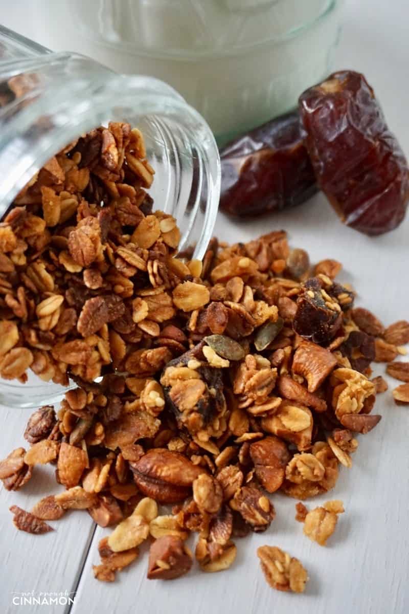 homemade baked honey granola pouring out of a mason jar onto a white table (honey granola recipe)