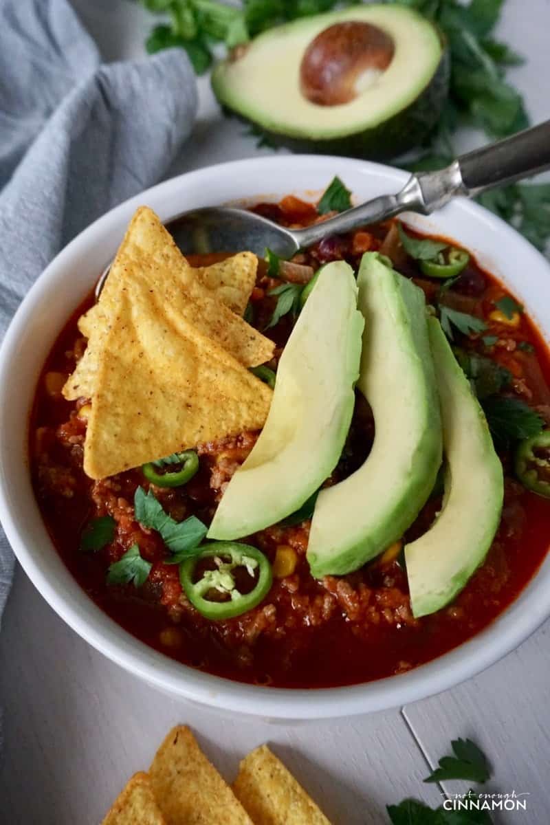 close-up of a bowl of turkey taco soup topped with avocado slices and nacho chips