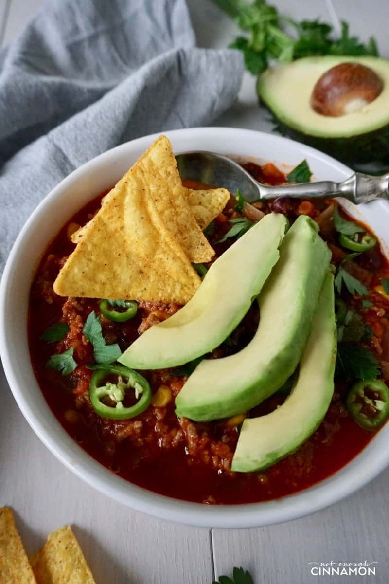 a bowl of turkey taco soup topped with nacho chips and avocado slices